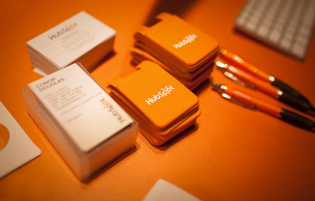 Detailaufnahme vom HubSpot-Stand mit Visitenkarten, Werbegeschenken und Kugelschreibern in leuchtendem Orange